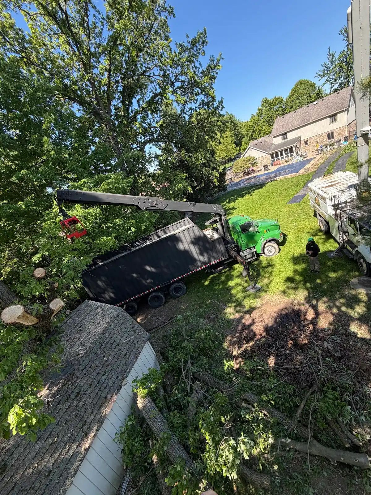 Black truck tipped on a grassy hillside near a stone wall, with debris and a green lawnmower nearby.
