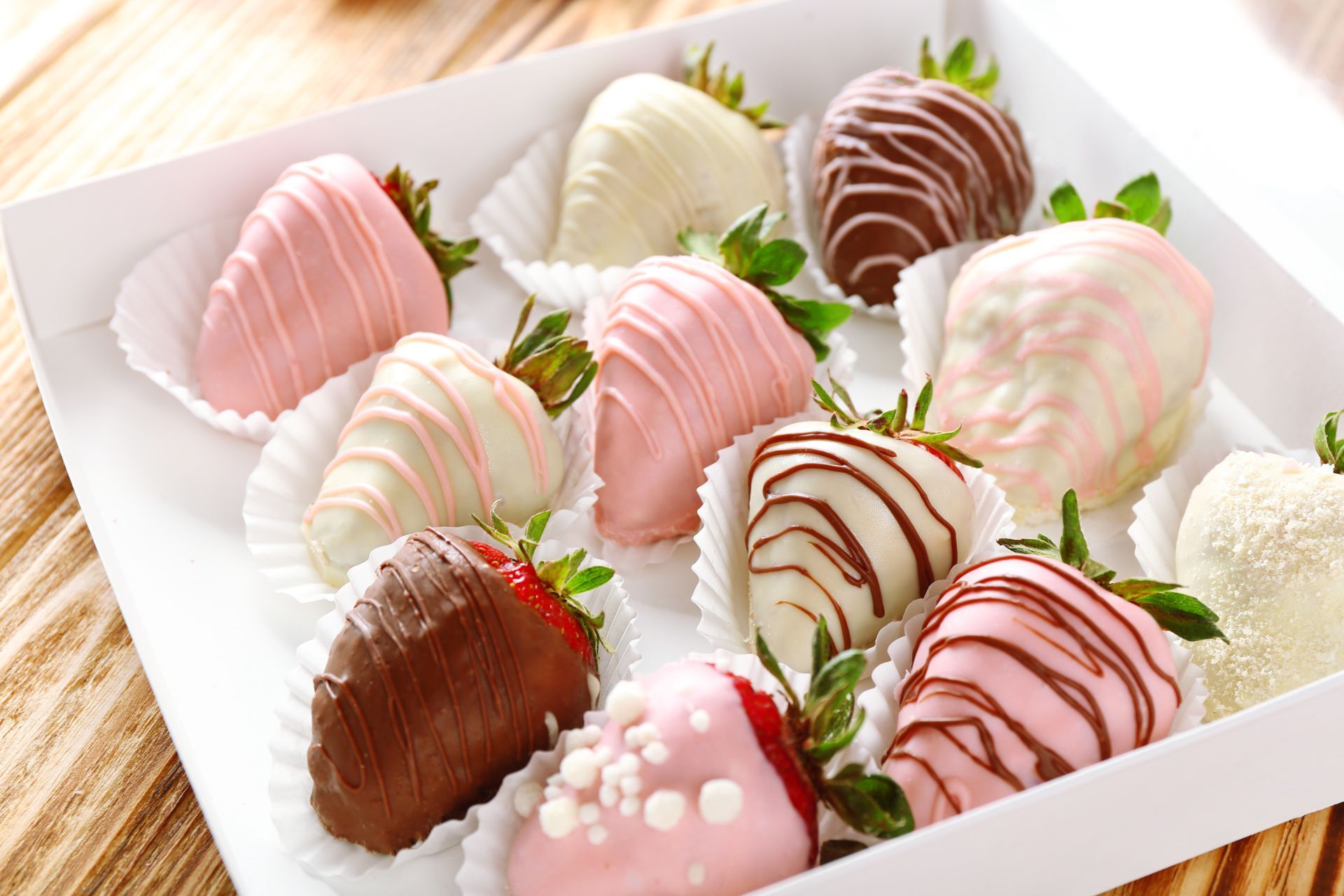 Assorted chocolate-covered strawberries in a white box on a wooden surface