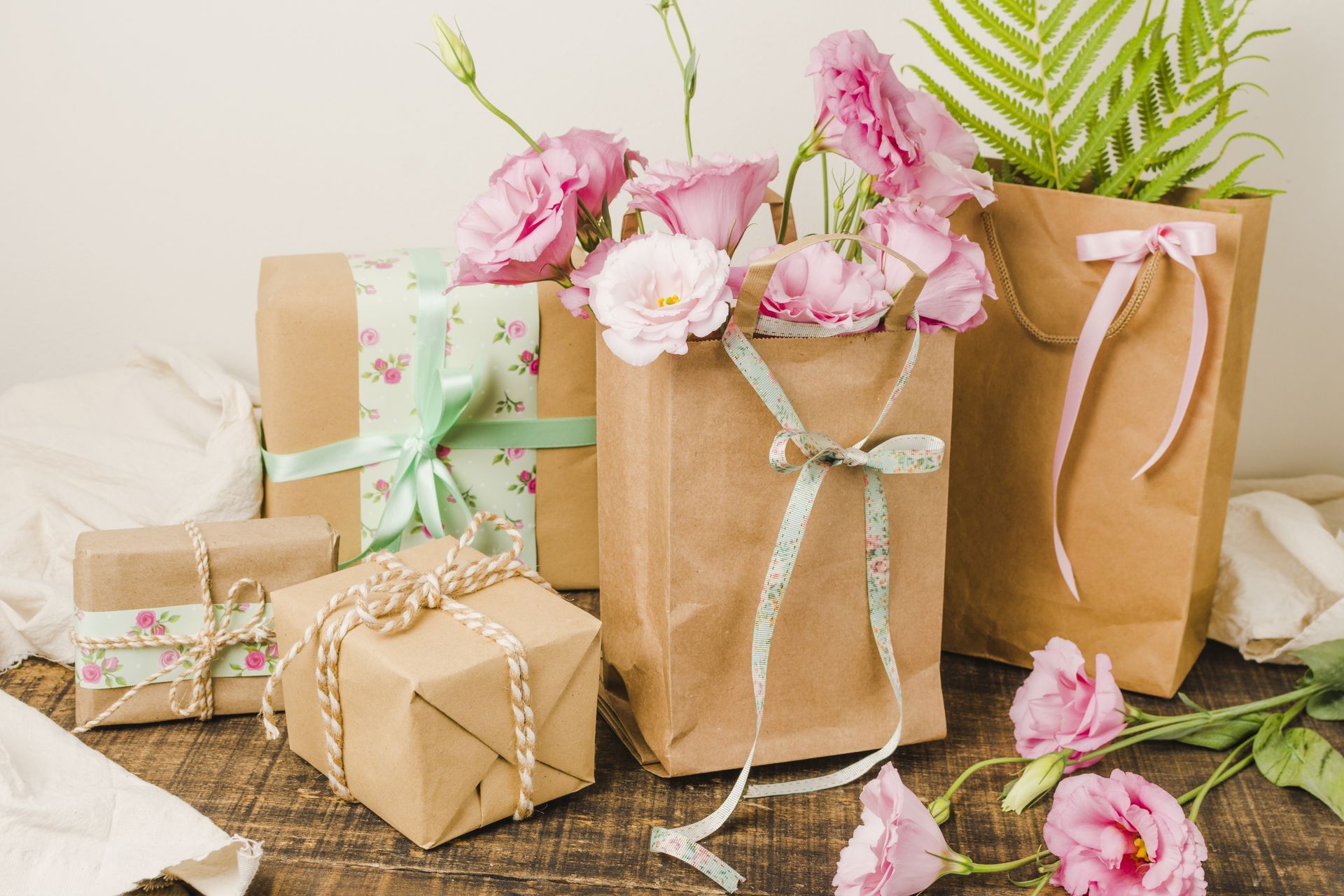 Wrapped gifts with pink flowers and greenery on a light background