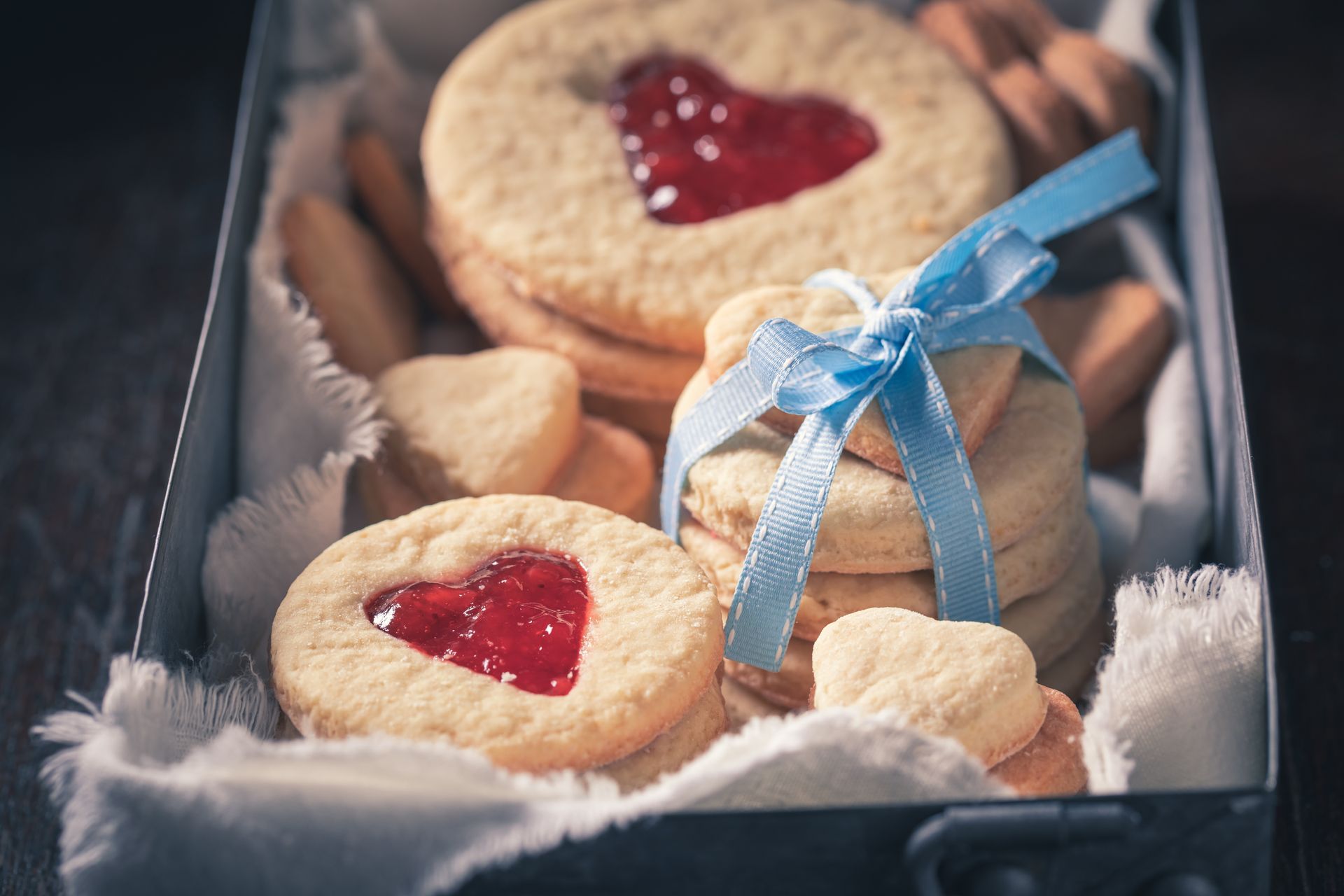 Gift box with jam-filled cookies, small cookies, and a blue ribbon on white fluff