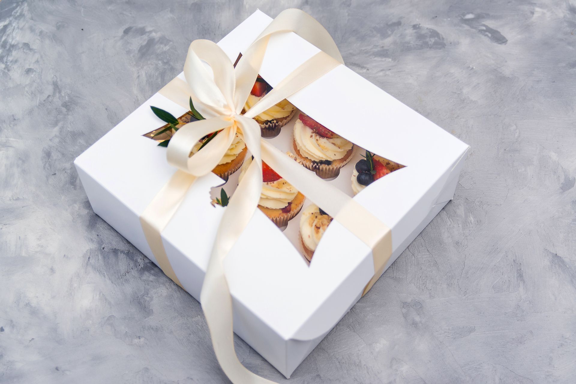 White gift box with gold ribbon and clear window showing pastries inside