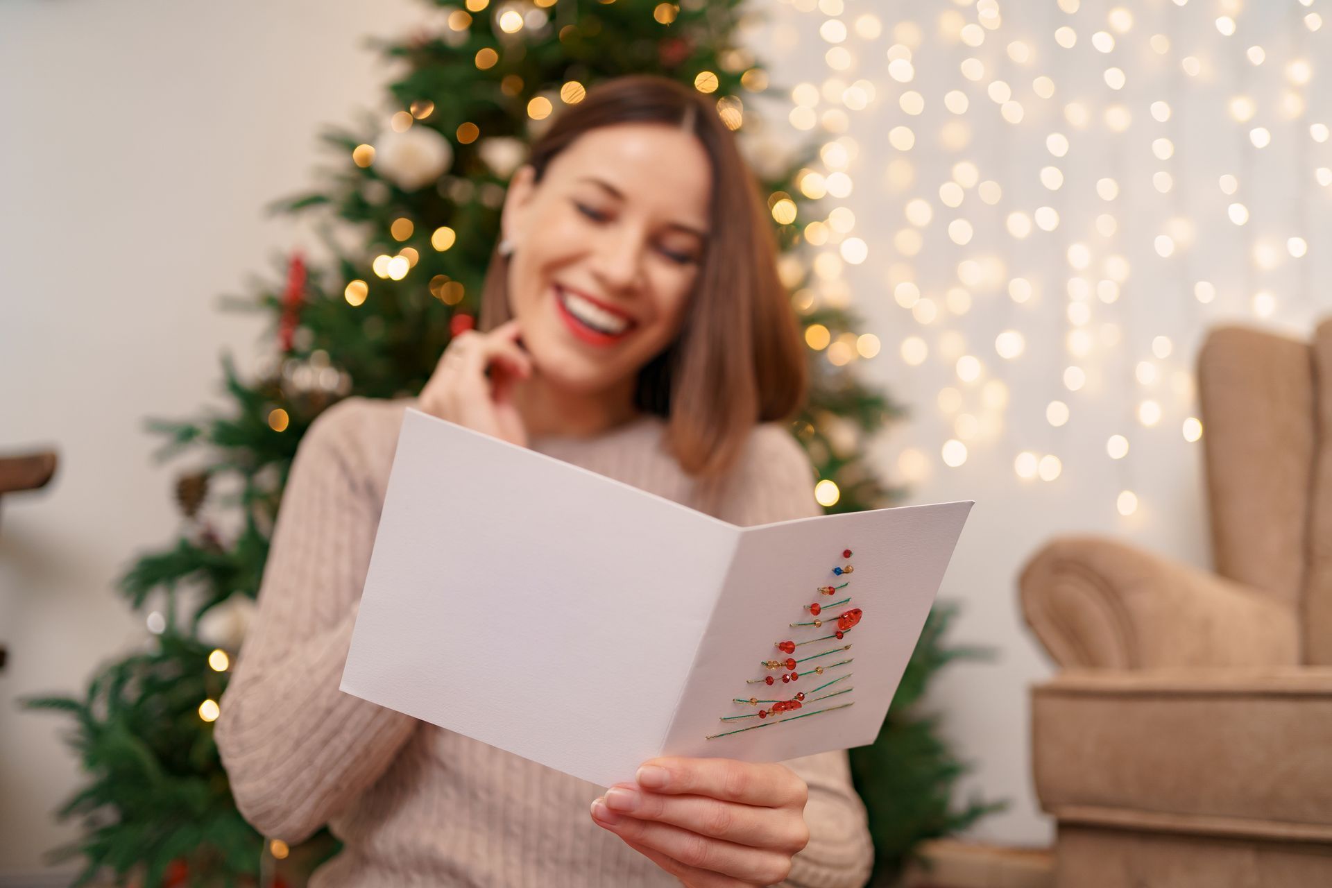 Smiling woman reading a Christmas card by a decorated tree and warm lights