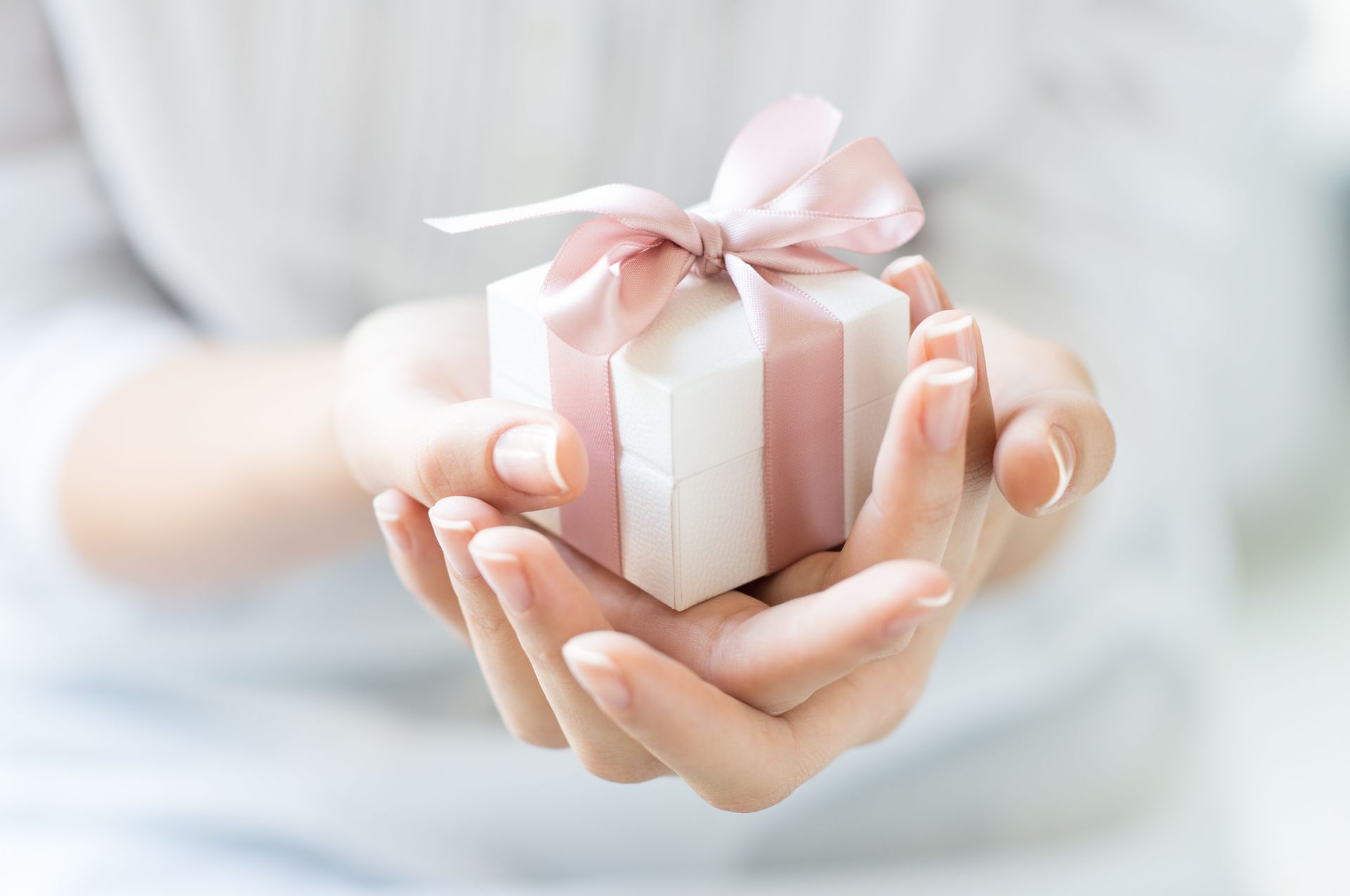 Hands holding a small white gift box with a pink ribbon and bow