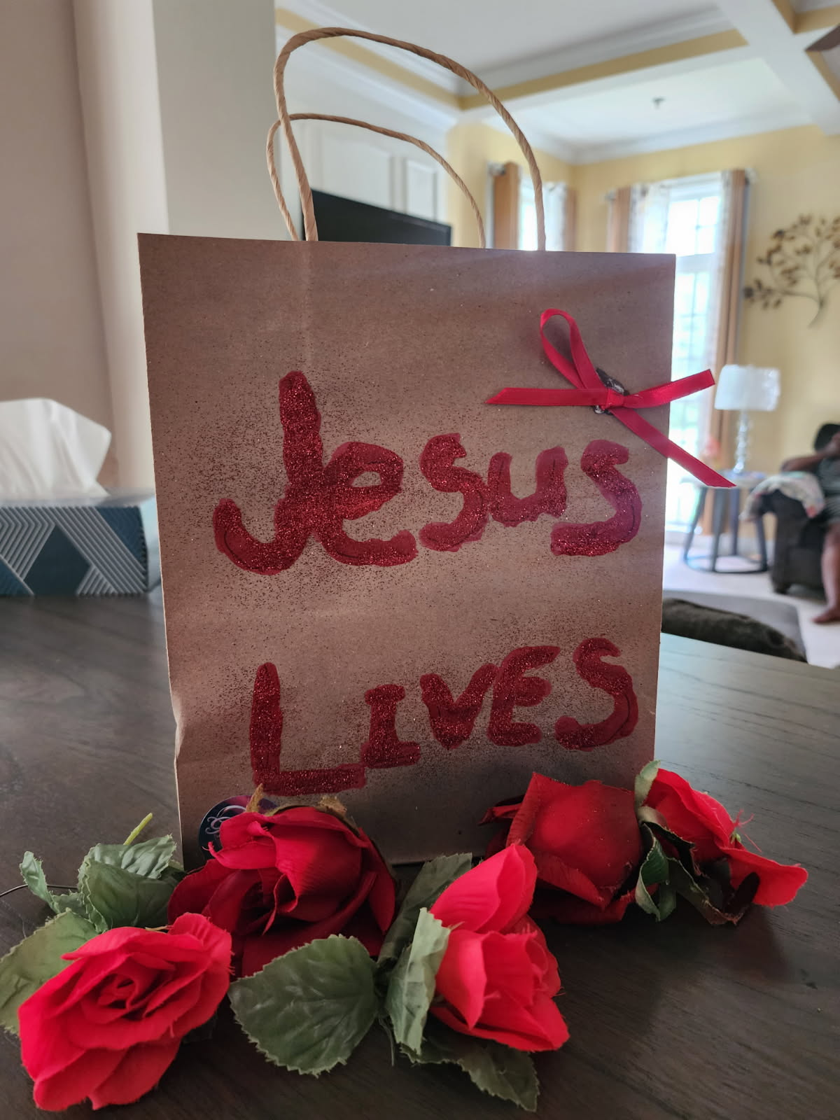 Gift bag with red “Jesus Loves” lettering and red roses on a table