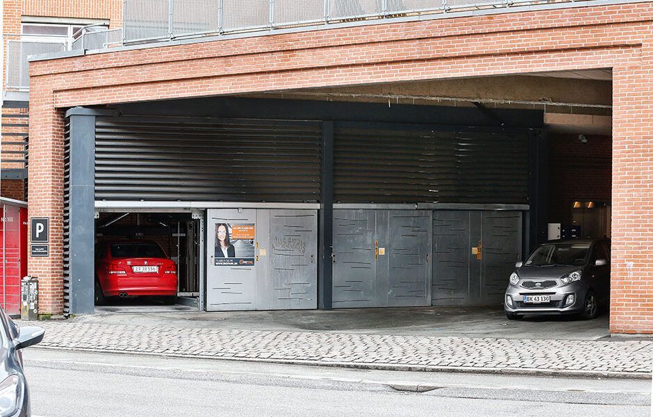 En rød bil er parkeret i en garage under en murstensbygning.