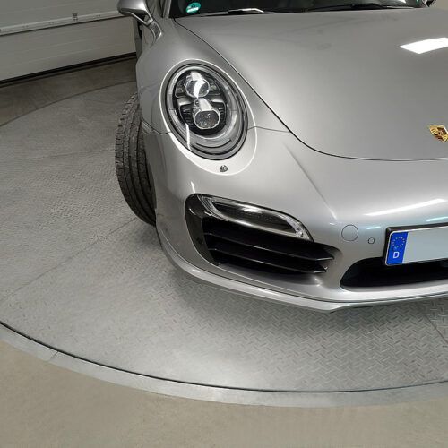 En sølv porsche er parkeret på en pladespiller i en garage.