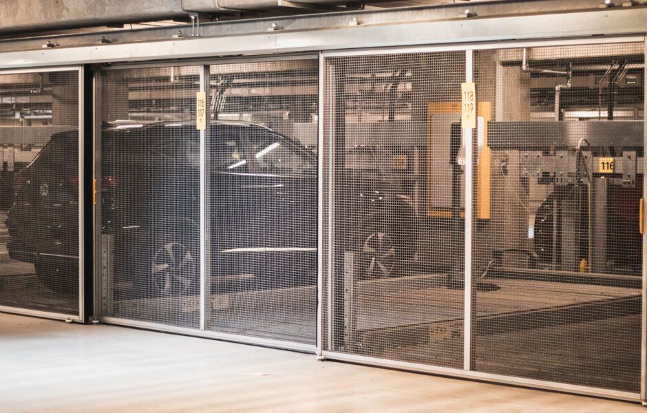 En bil er parkeret i et parkeringshus bag en glasskydedør.
