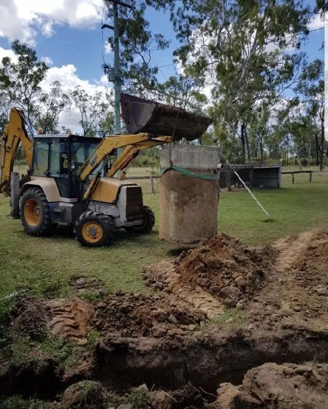 Yellow Backhoe Moving a Concrete Structure in a Grassy Field — MCA Plumbing & Drainage in Jensen, QLD