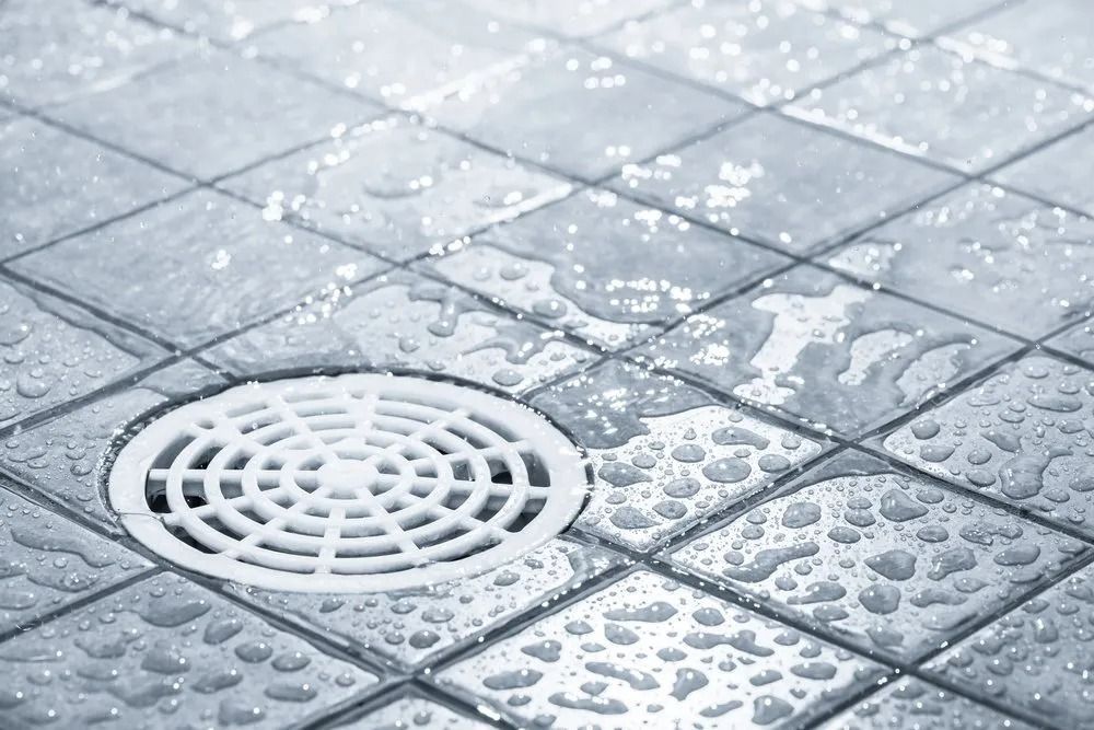 Wet, Tiled Floor With a White Drain in the Center, and Water Droplets — MCA Plumbing & Drainage in Jensen, QLD