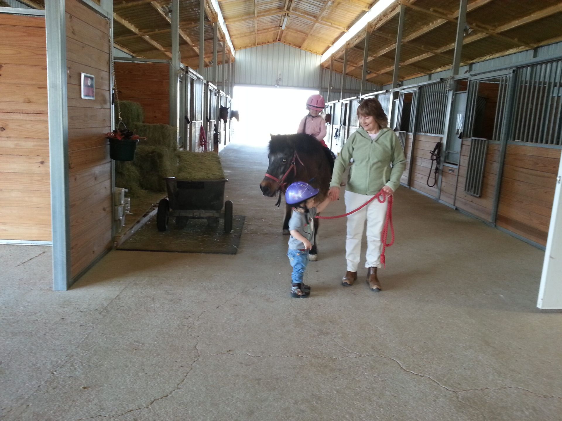 A woman and child are walking a horse in a barn - Anna, TX - Spirit Song Youth Equestrian Academy