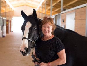 Alison Selby - Anna, TX - Spirit Song Youth Equestrian Academy A woman is standing next to a black horse in a stable.