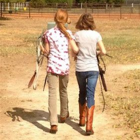 Two young girls are walking down a dirt path with a horse.