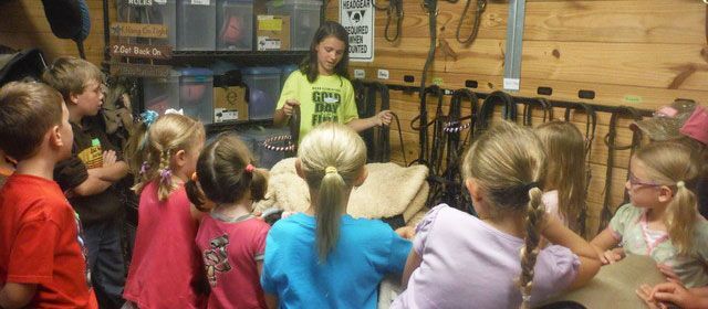 A girl in a yellow shirt is talking to a group of children - Anna, TX - Spirit Song Youth Equestrian Academy