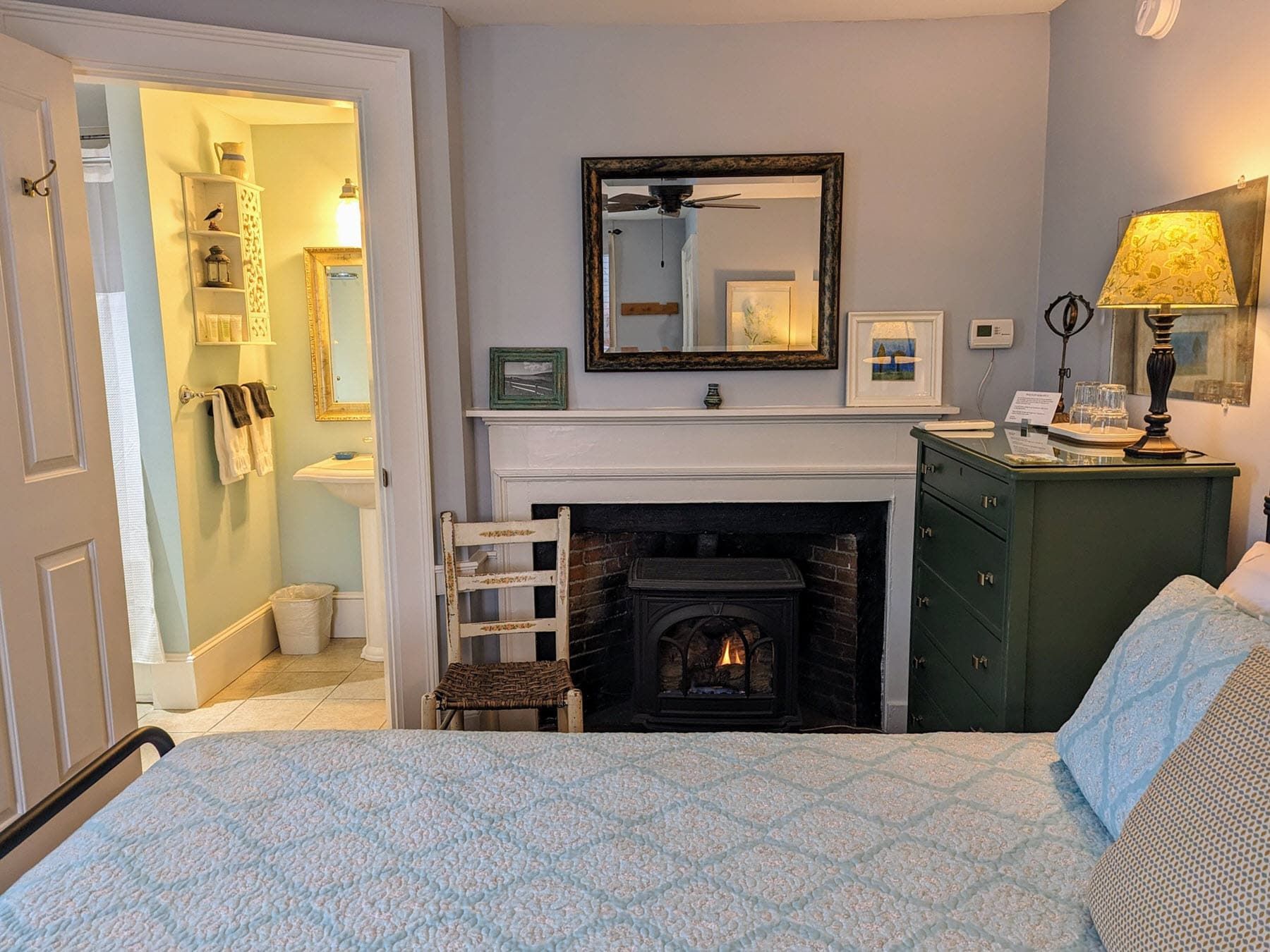 A bedroom with a bed , dresser , fireplace and mirror.