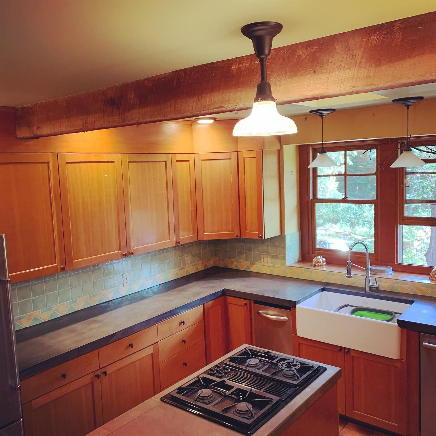 Kitchen with wood cabinets, island with stove, farmhouse sink, and windows.
