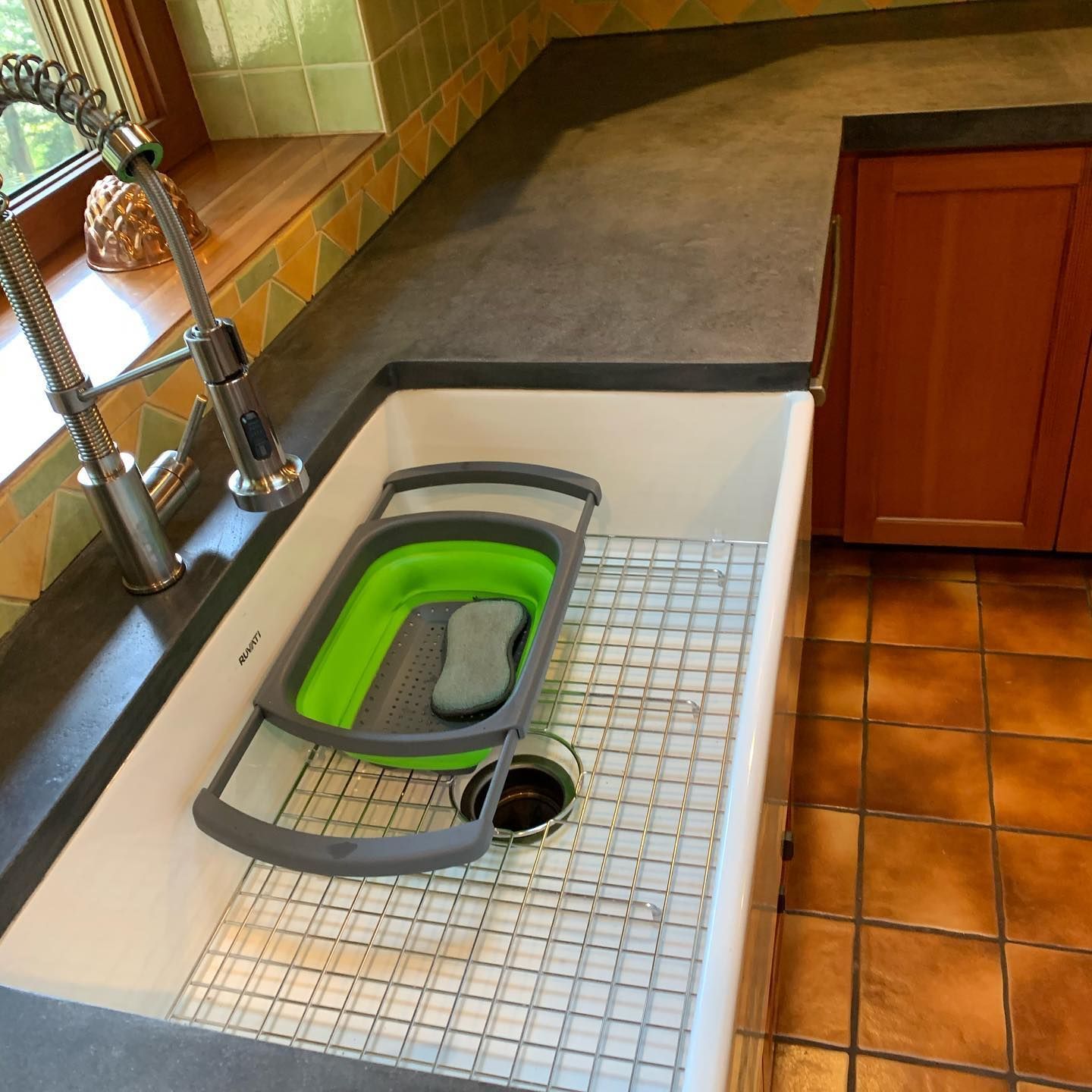 Kitchen sink with a collapsible dish rack and sponge; grey countertop and orange cabinets.