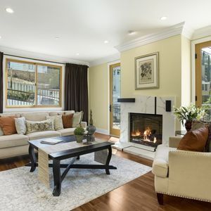 Cozy living room with fireplace, light-colored furniture, and large windows, wood floors and cream walls.