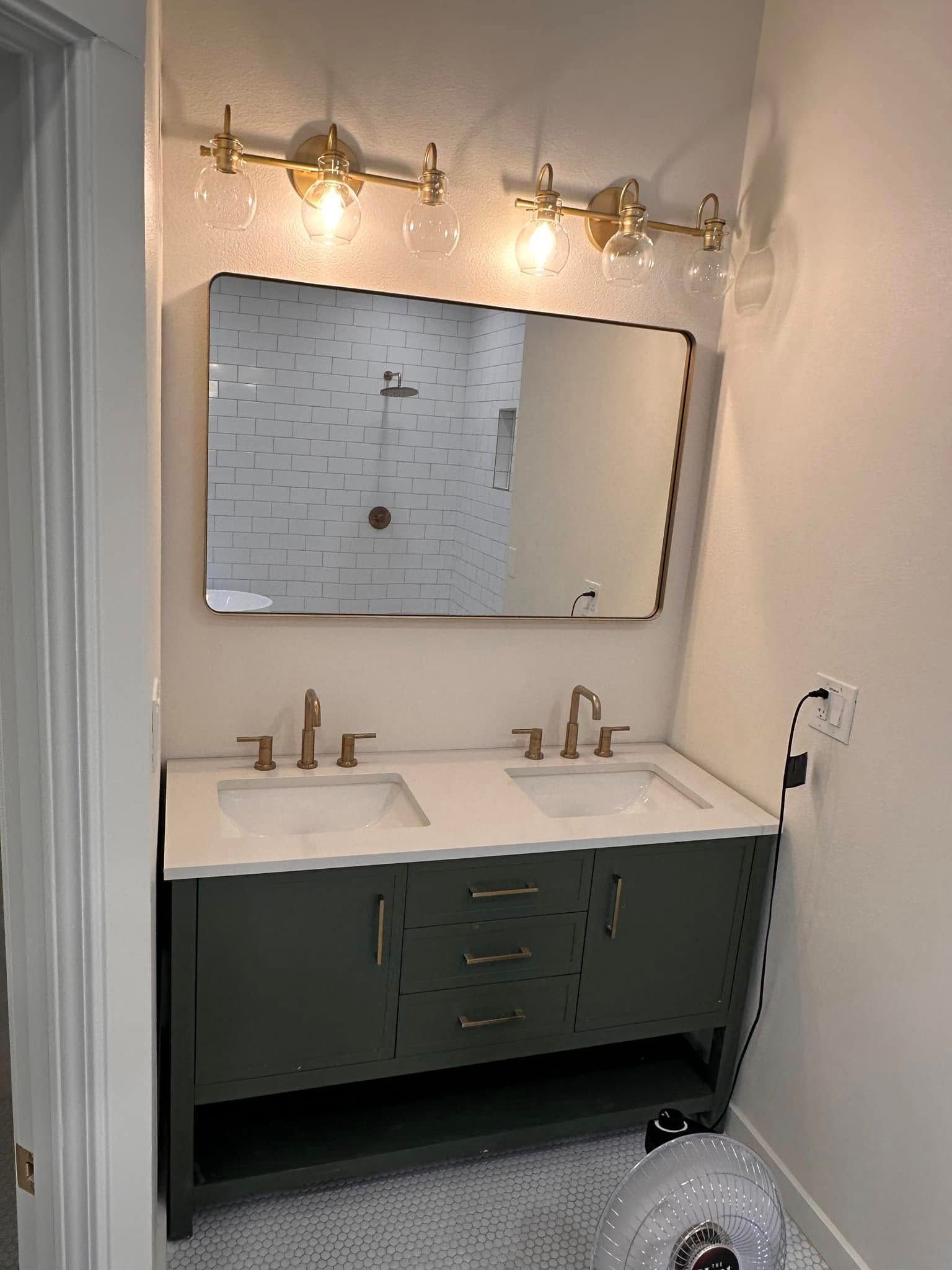 Bathroom with green vanity, double sinks, gold fixtures, large mirror, and gold light fixtures above.