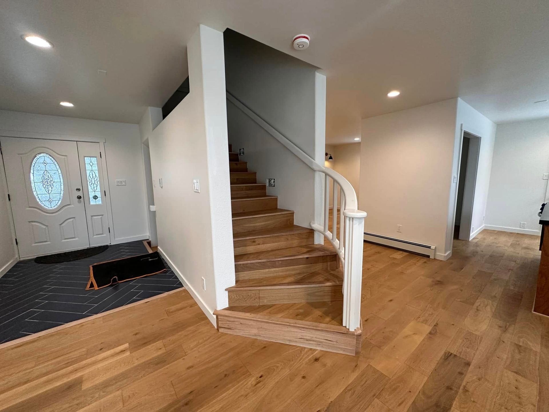 Entryway with staircase, wooden floors, white walls, and a front door.