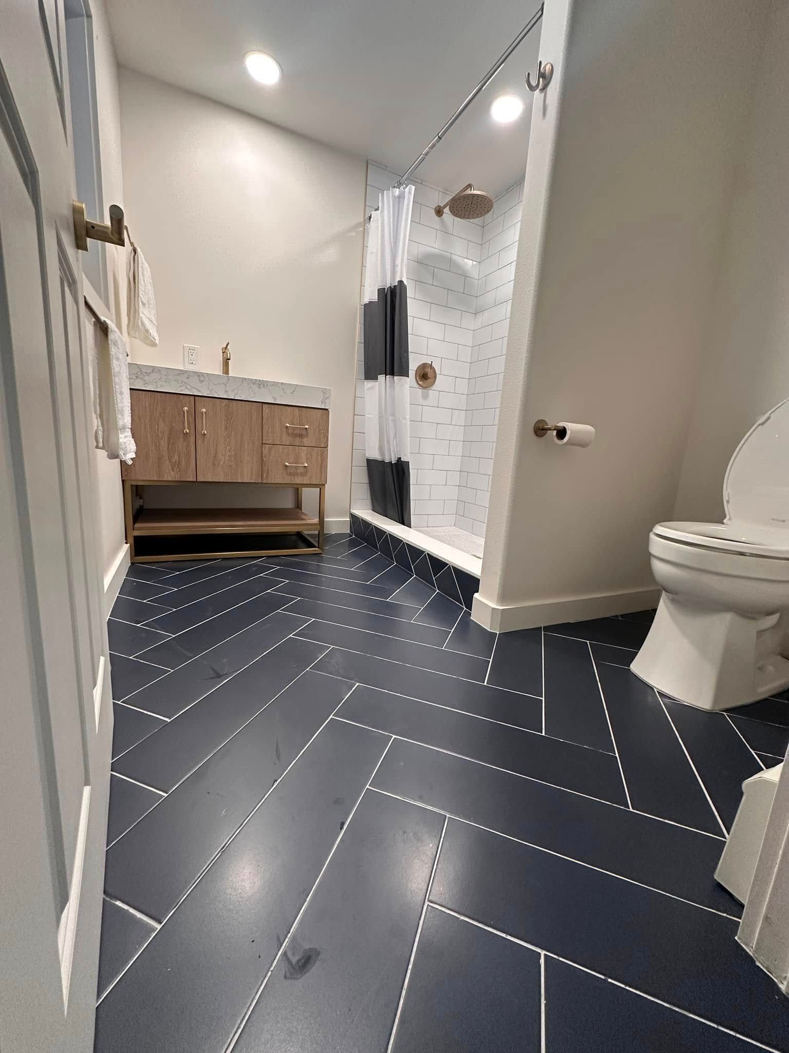 Modern bathroom with navy herringbone tile, white walls, wood vanity, and glass shower.