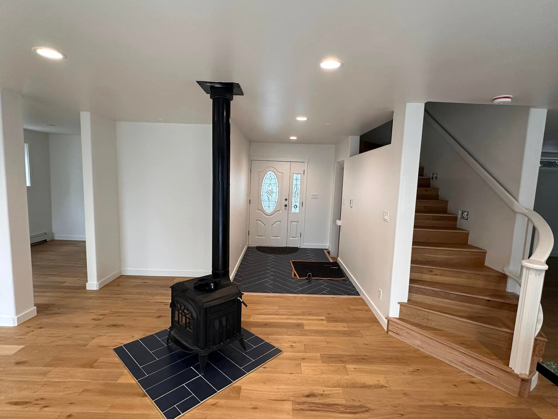 An entryway with hardwood floors, a black stove, white walls, and a staircase.