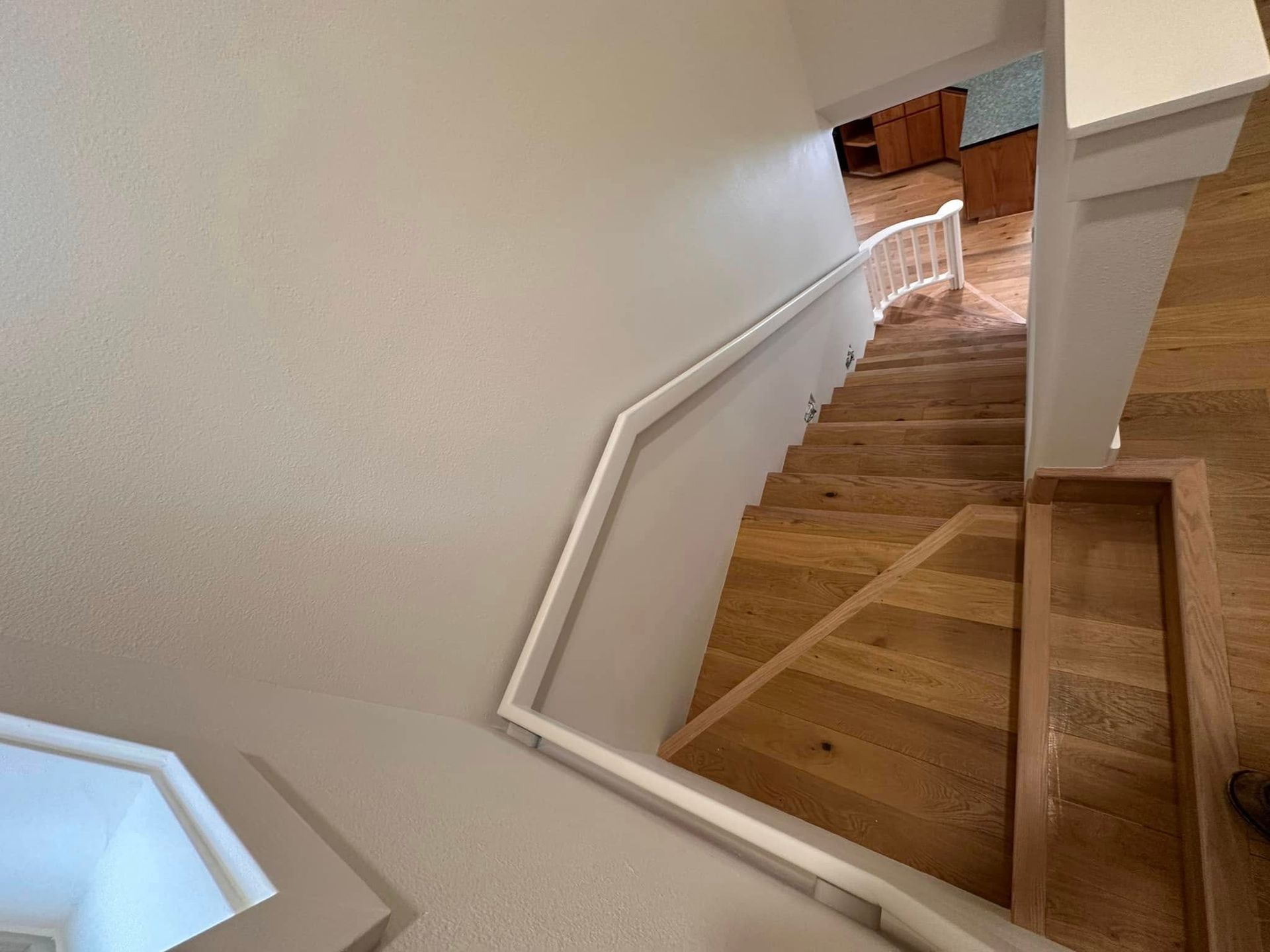 Wooden staircase with white railing descending from a beige wall.