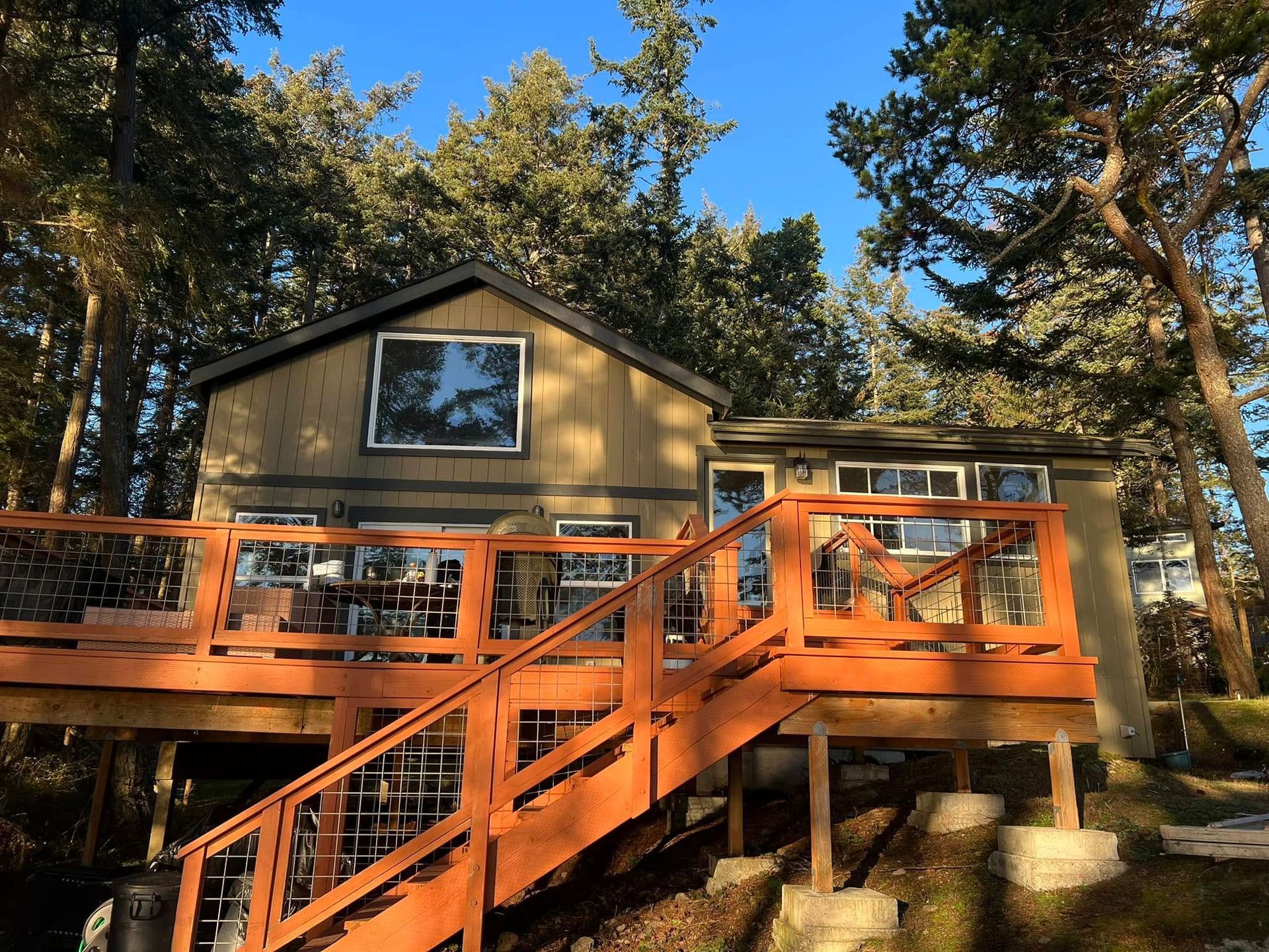 Cabin with orange deck and stairs surrounded by trees under a blue sky.