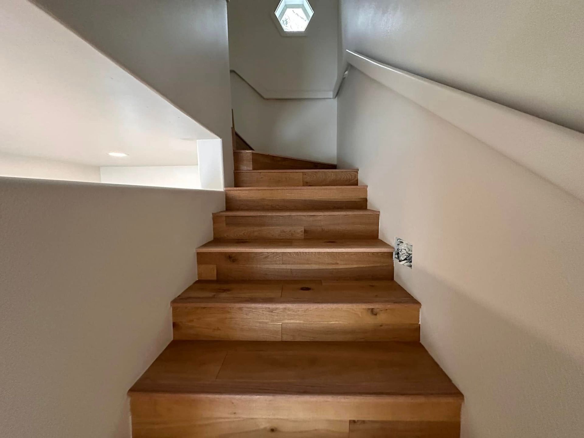 Wooden staircase with white walls and a ceiling light.