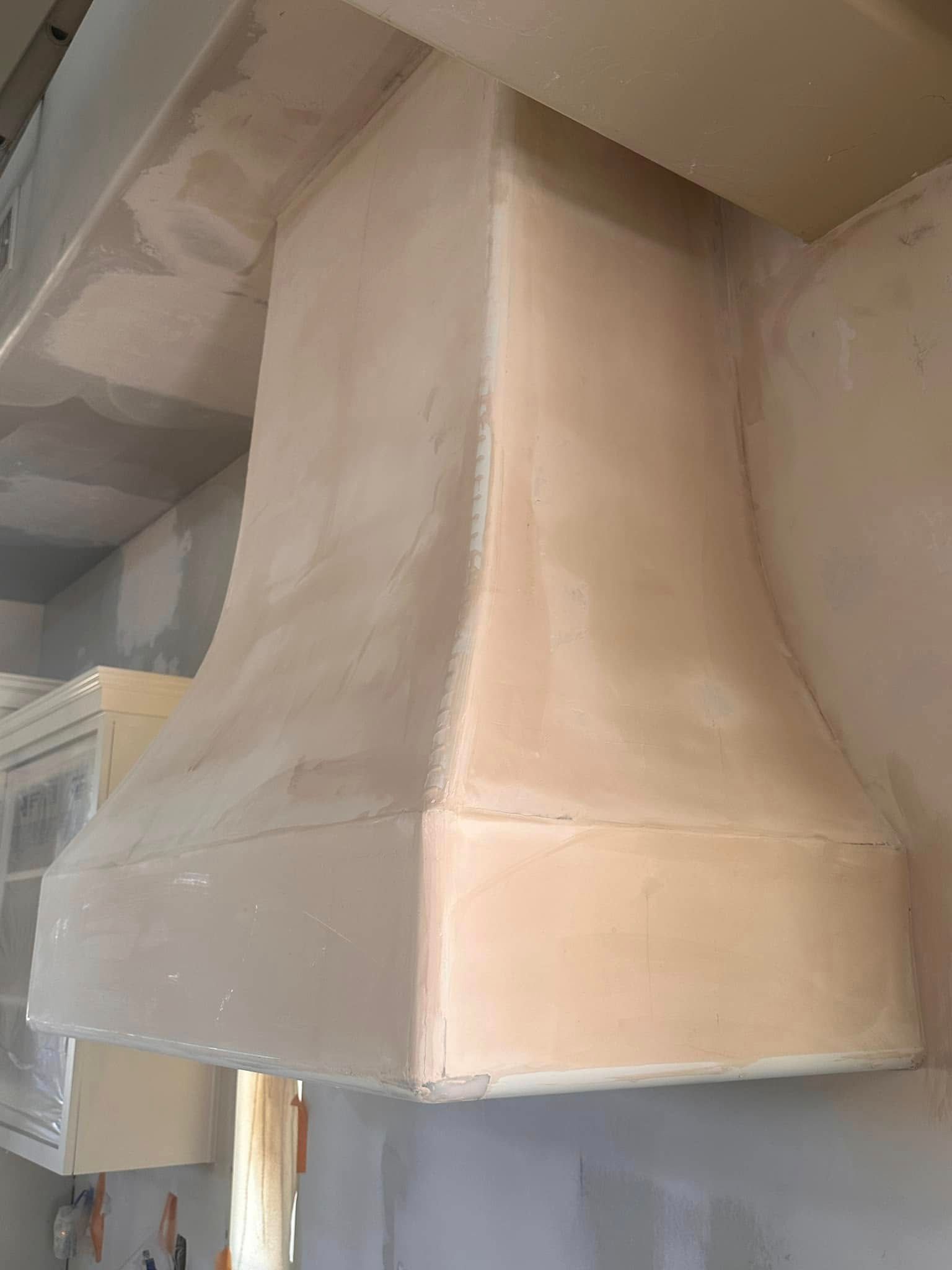 Cream-colored kitchen range hood, newly constructed and textured, installed over a countertop.
