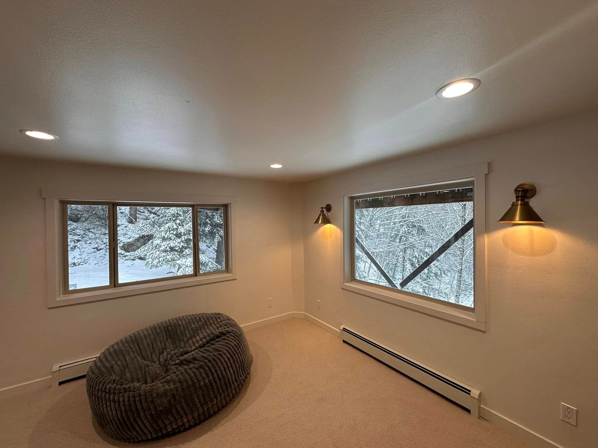Cozy room with beanbag, windows with snowy view, warm sconce lighting. Beige walls and carpet.