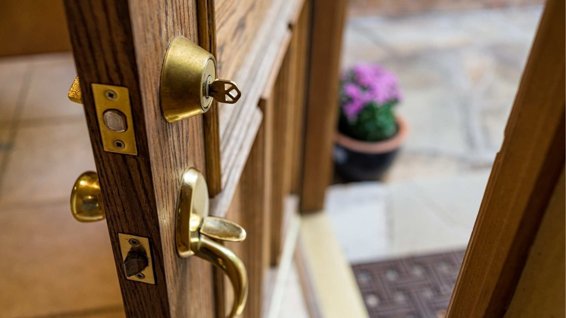 Door ajar, showing gold doorknob and lock, leading to a glimpse of a plant and stone floor.