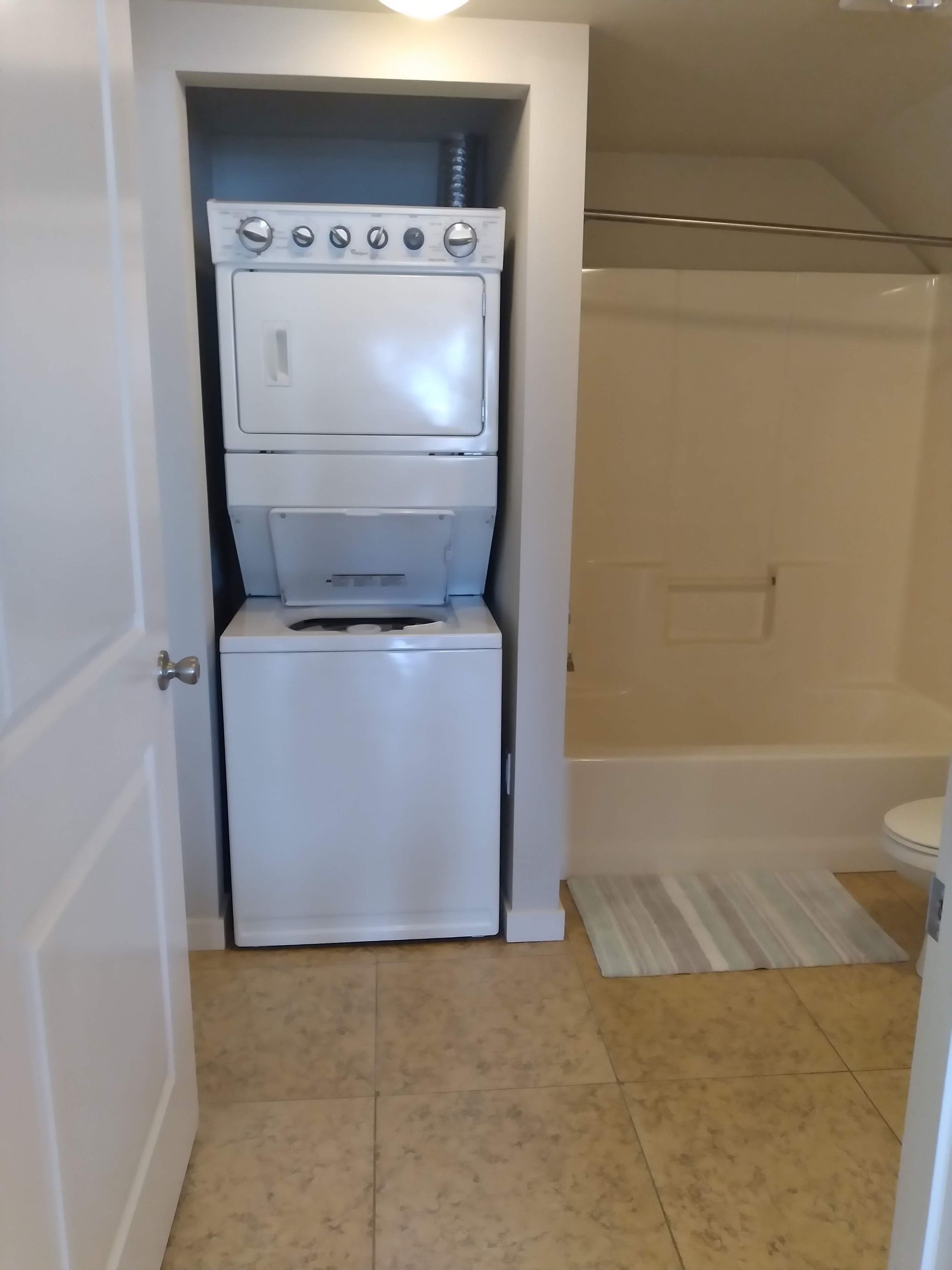 Stacked washer and dryer in a narrow bathroom beside a bathtub