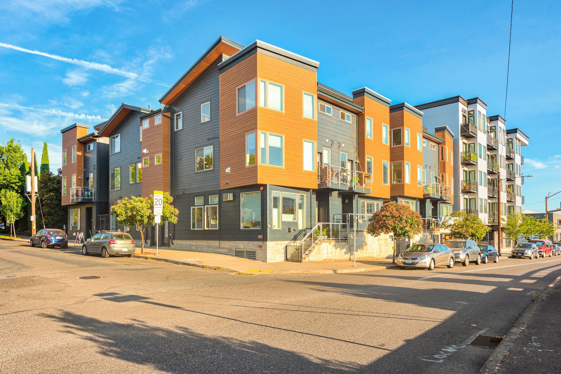 Modern apartment building on a sunny street corner with parked cars and balconies