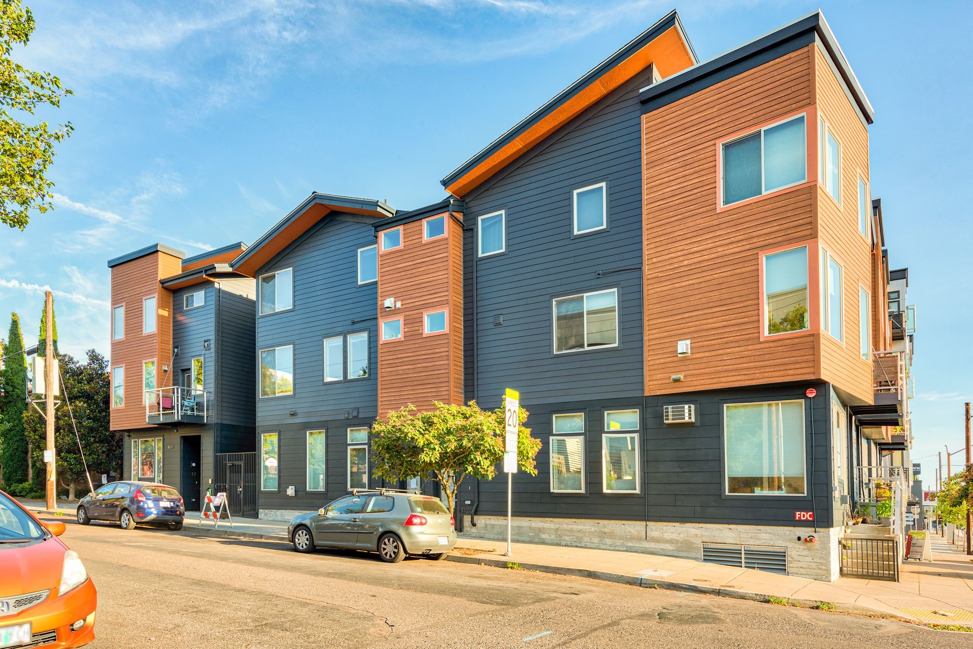 Modern apartment building with wood and dark gray siding, parked cars, and blue sky