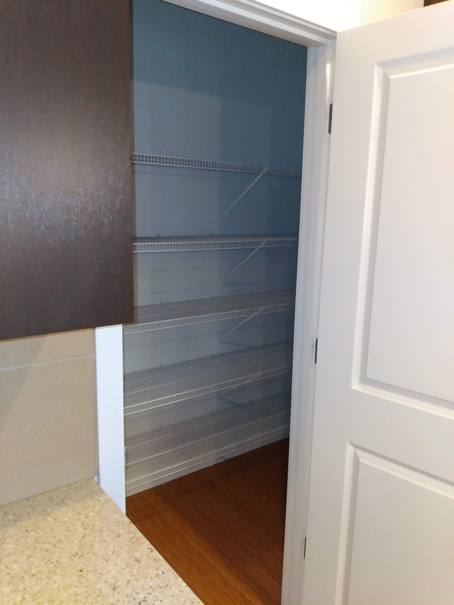 Open closet with wire shelves, blue walls, and white double doors on a wooden floor