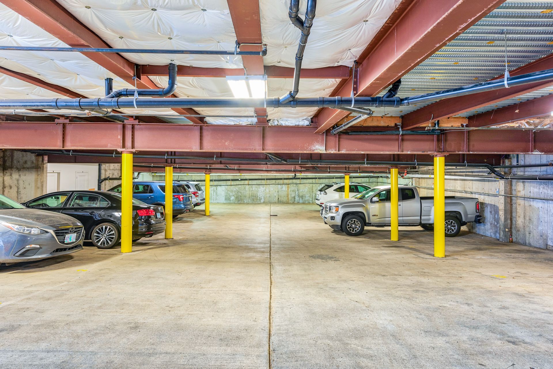 Underground parking garage with cars, yellow support columns, and exposed pipes on the ceiling