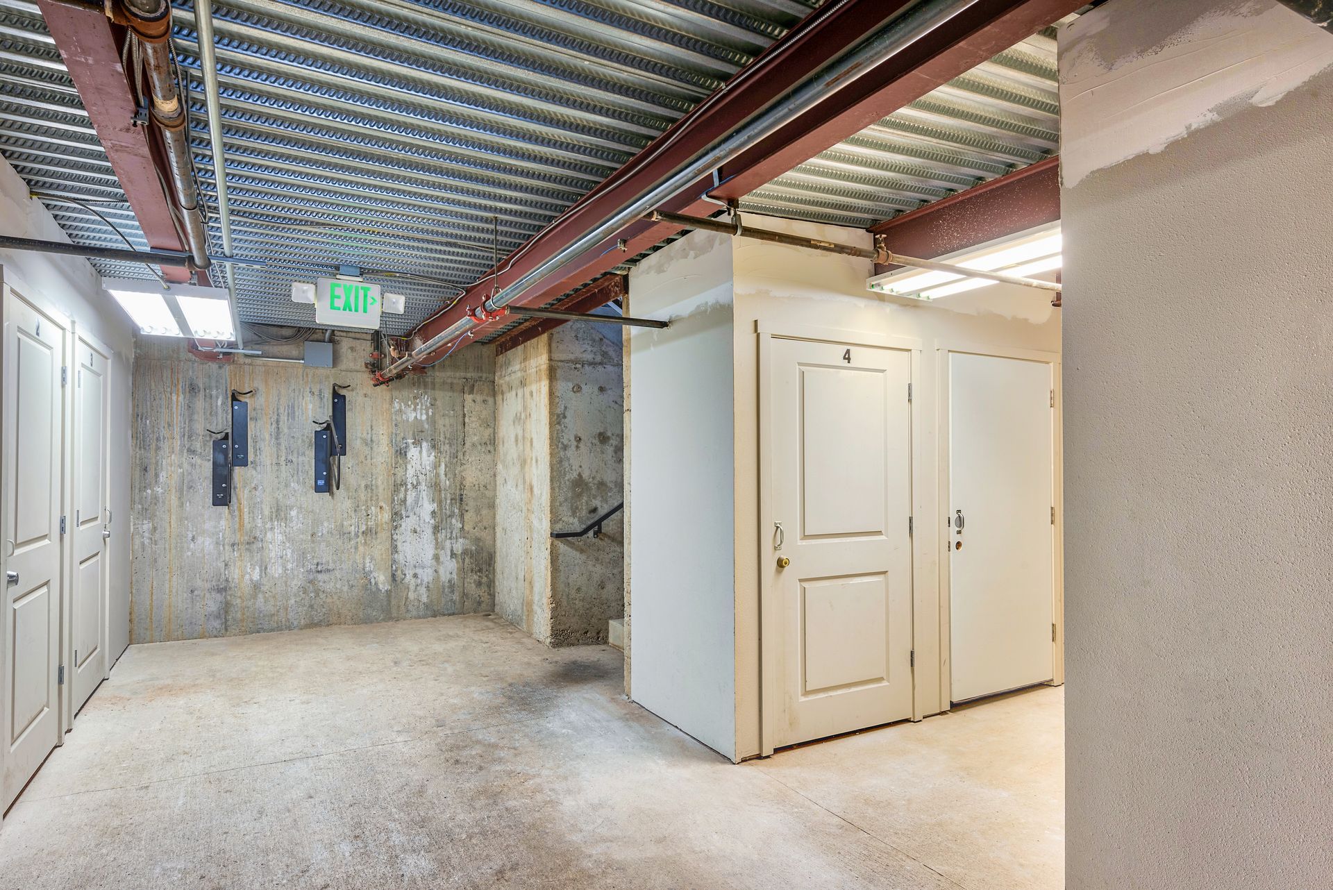 Empty industrial hallway with concrete walls, white doors, and exposed ceiling pipes and beams