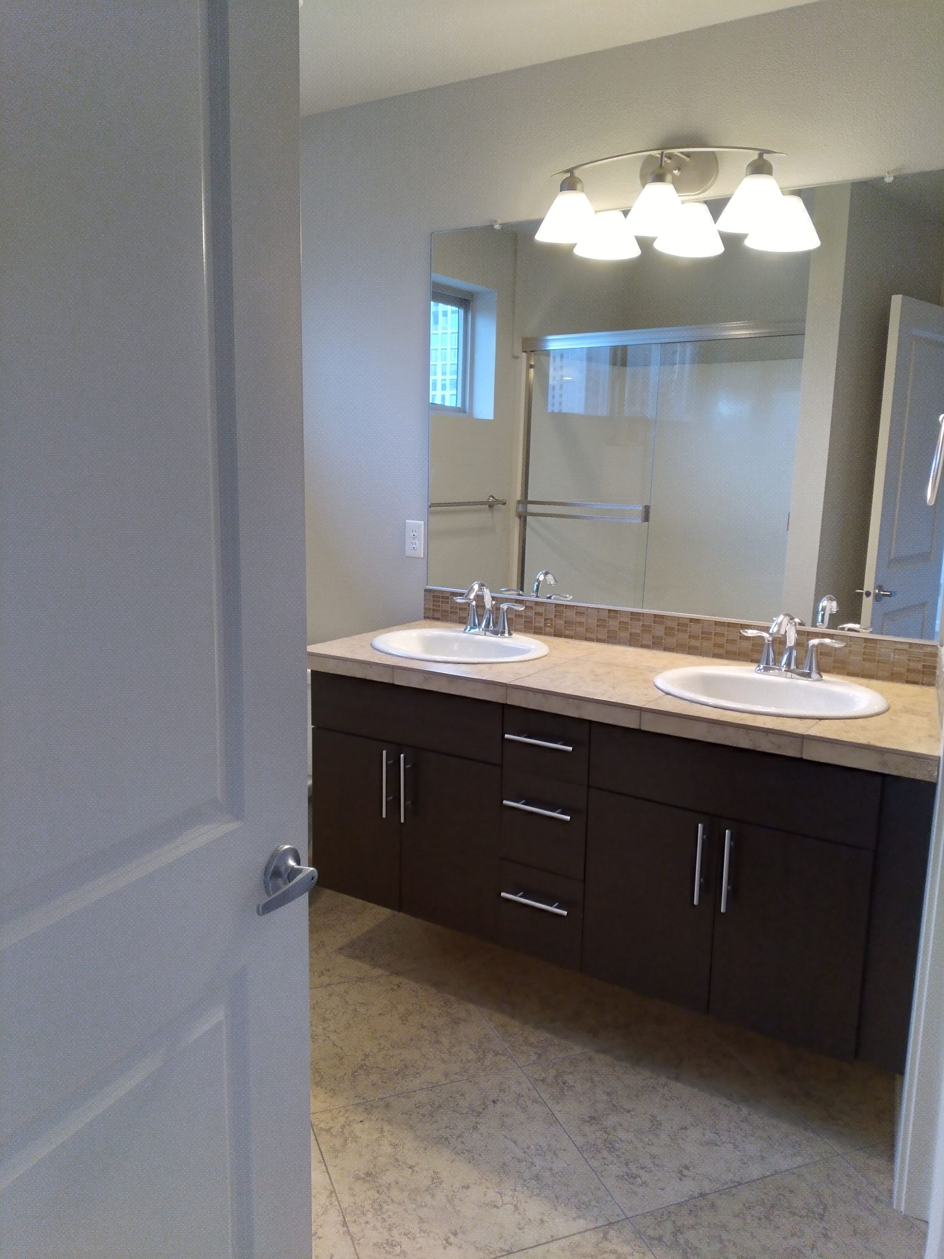 Modern bathroom vanity with double sinks, dark cabinets, large mirror, and overhead lights