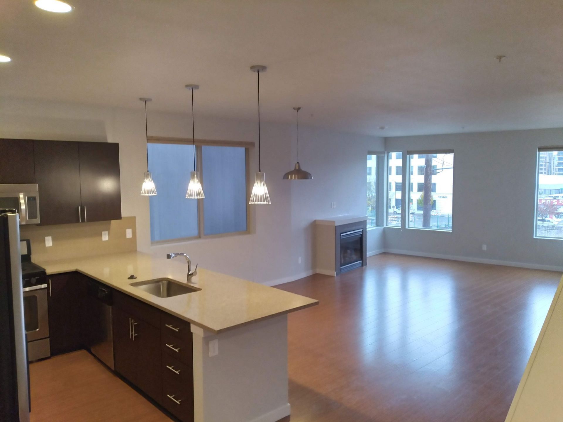 Open-plan kitchen and living room with pendant lights, island, hardwood floors, and large windows.