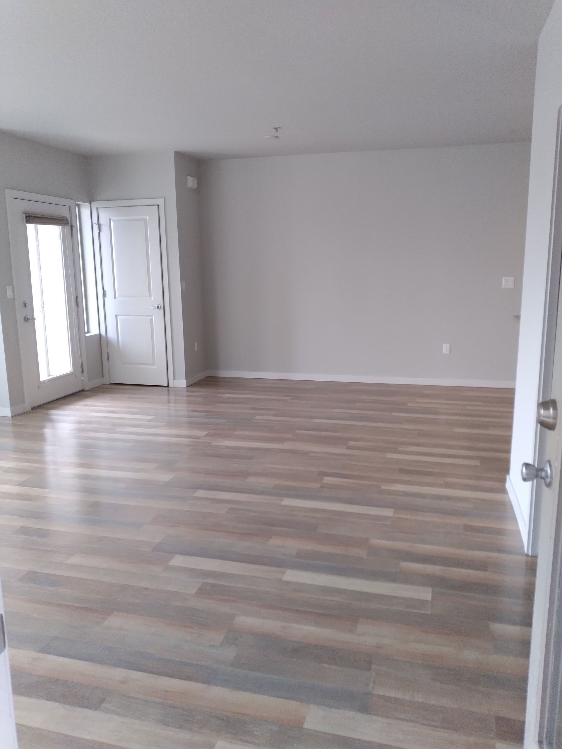 Empty unfurnished living room with wood flooring and open doors to a hallway