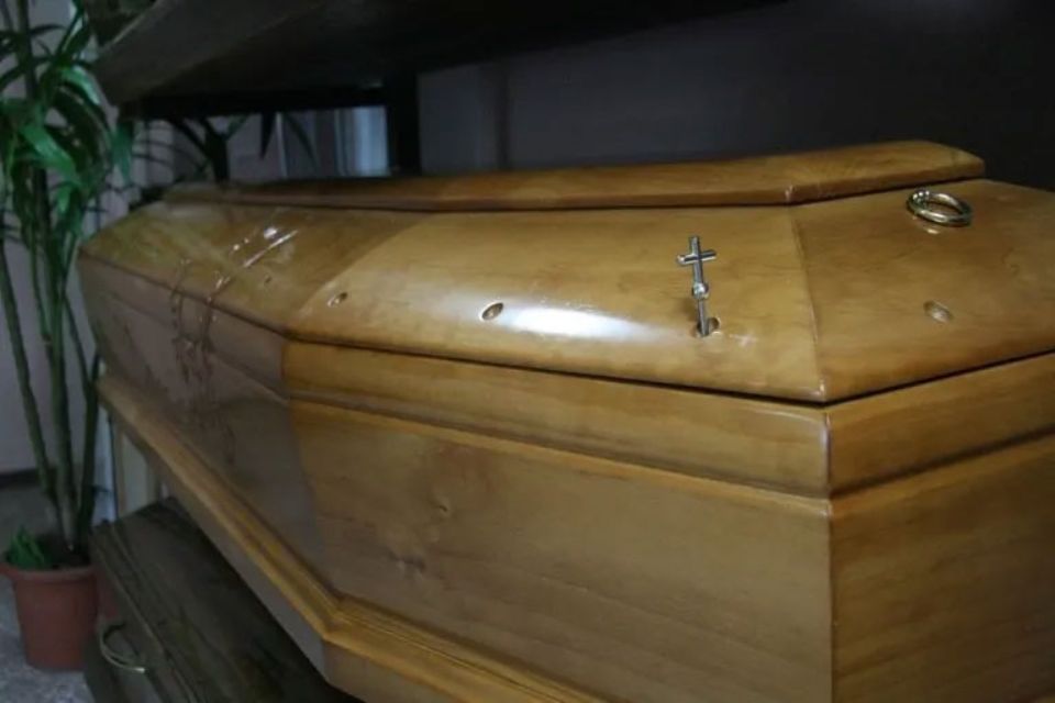 Una bara di legno con una croce sul coperchio è appoggiata su un tavolo.