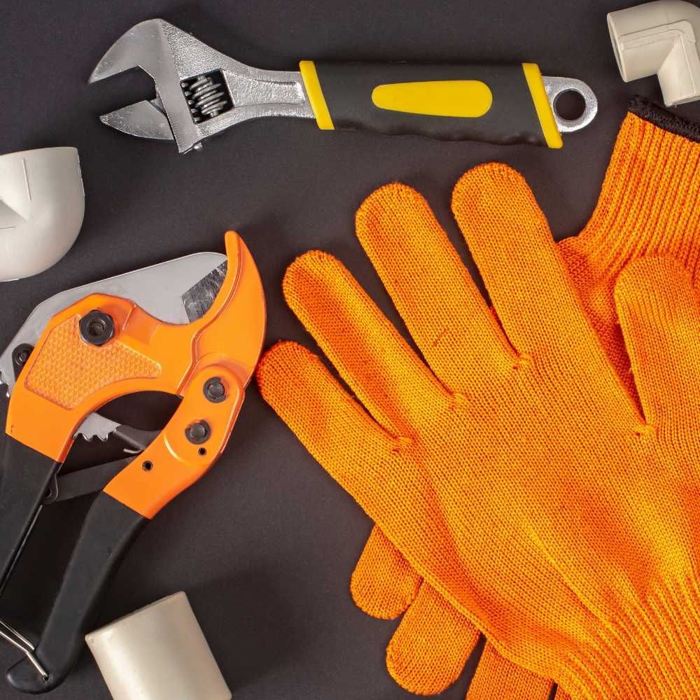 A pair of orange gloves laying next to a wrench