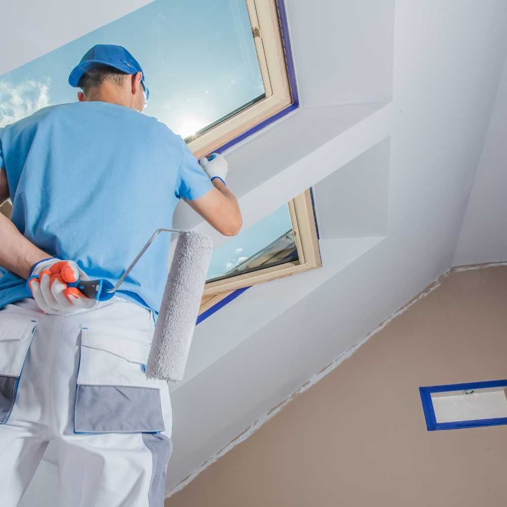 A man is standing on a ladder painting a window.