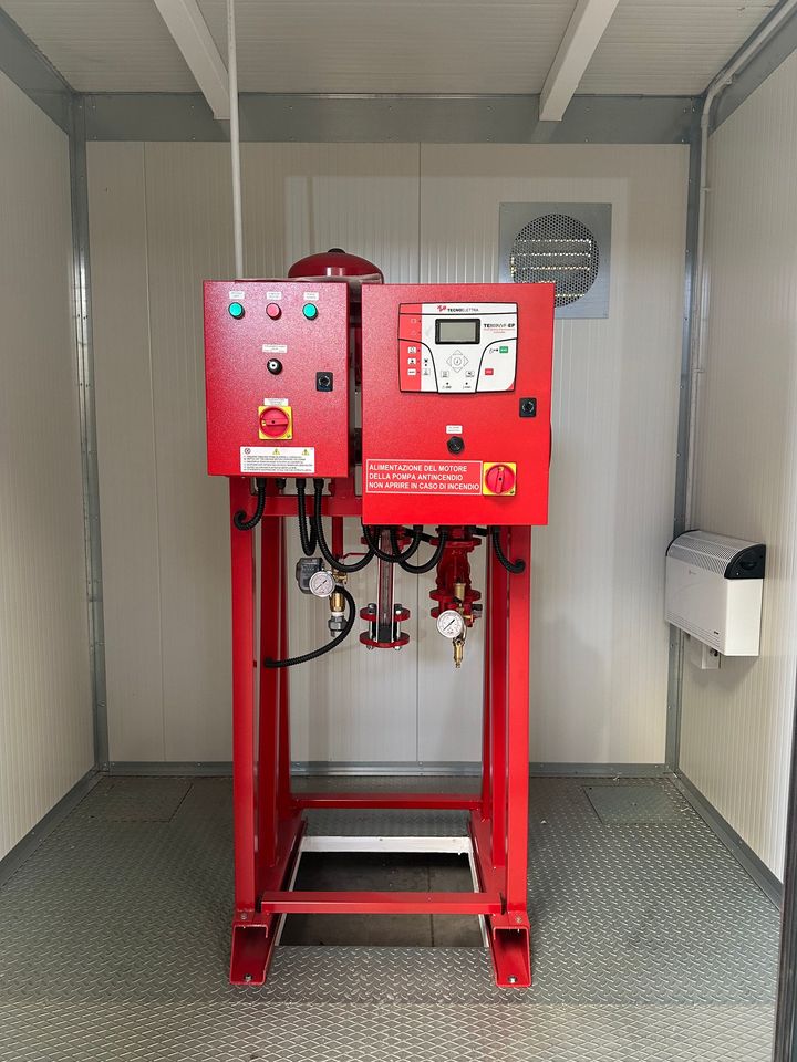 Macchina di controllo industriale rossa con manometri e tubi flessibili all'interno di un piccolo involucro metallico.