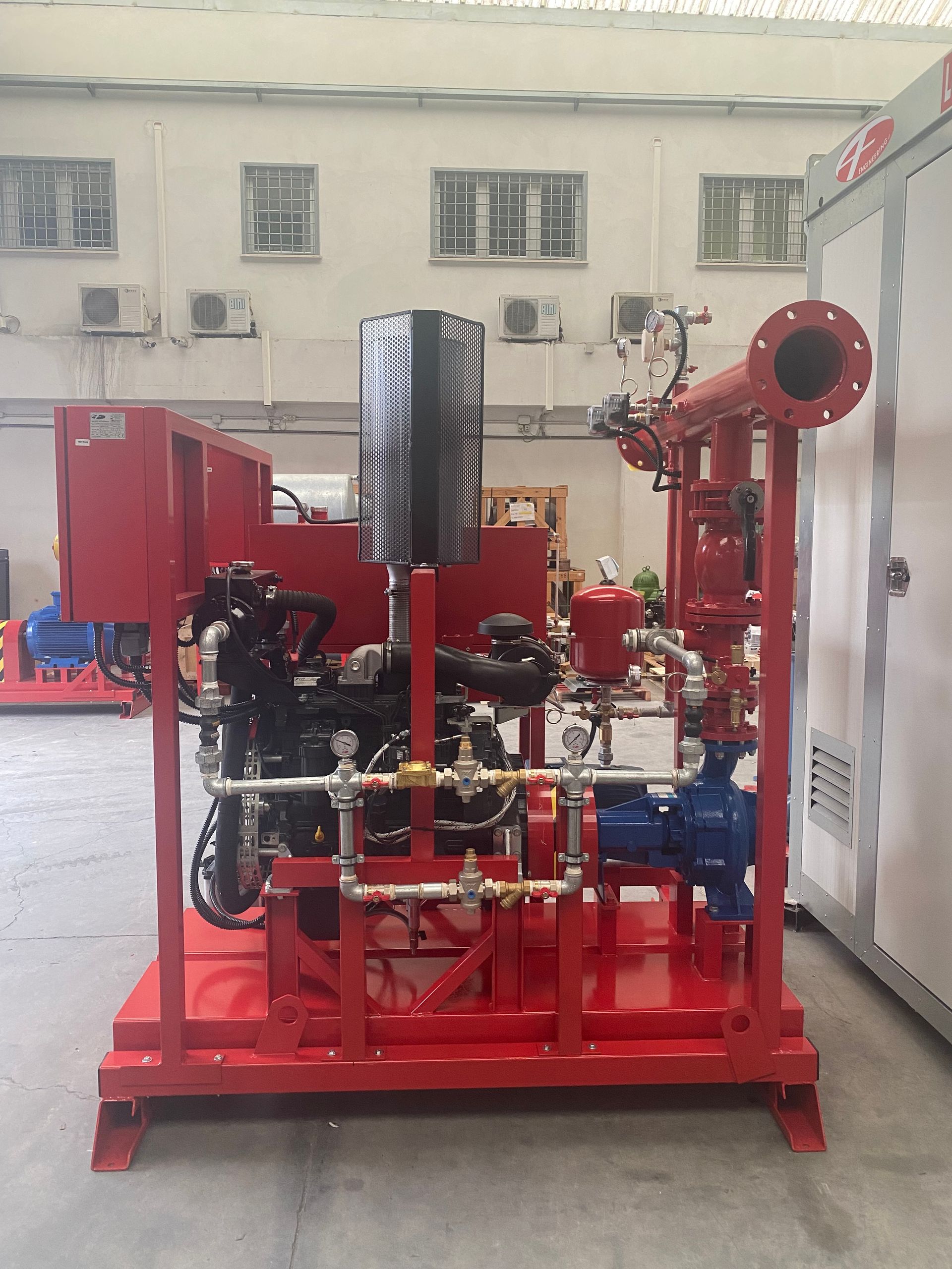 Macchinario industriale rosso con tubi, valvole e un grande pneumatico montato su una base rossa in un'officina.