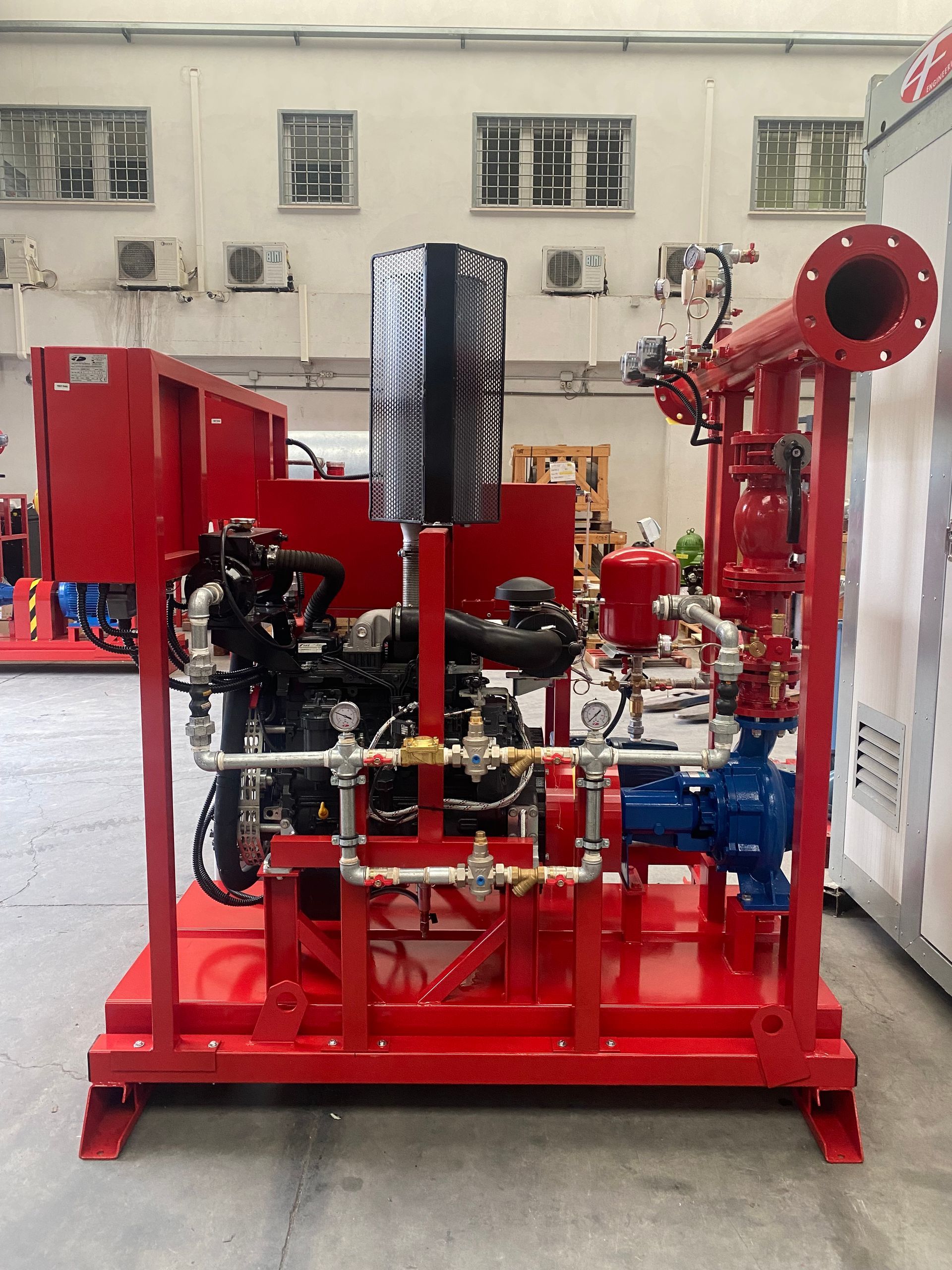 Sistema di pompaggio industriale rosso con tubi, valvole e motore montato su una slitta rossa in un'officina.