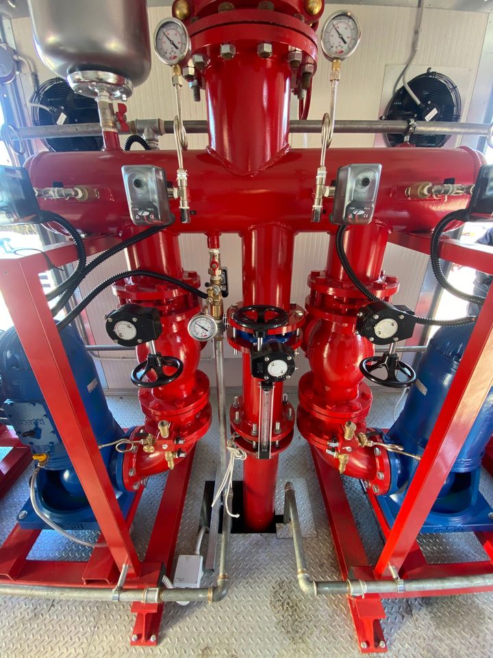 Tubazioni e valvole industriali rosse all'interno di un locale tecnico, con manometri e supporti metallici.