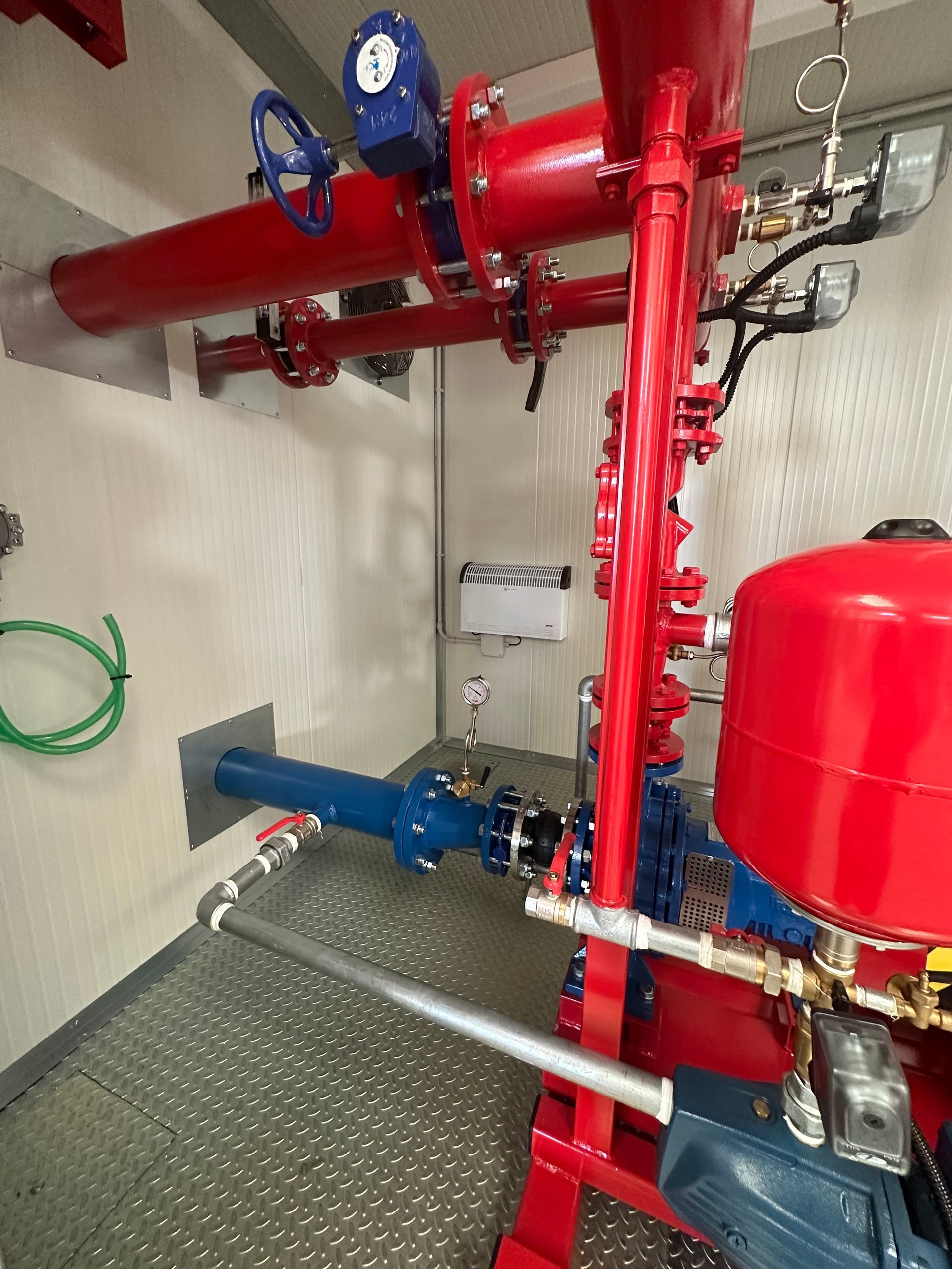 Tubature e valvole industriali rosse e blu su una piattaforma metallica all'interno di un locale tecnico.