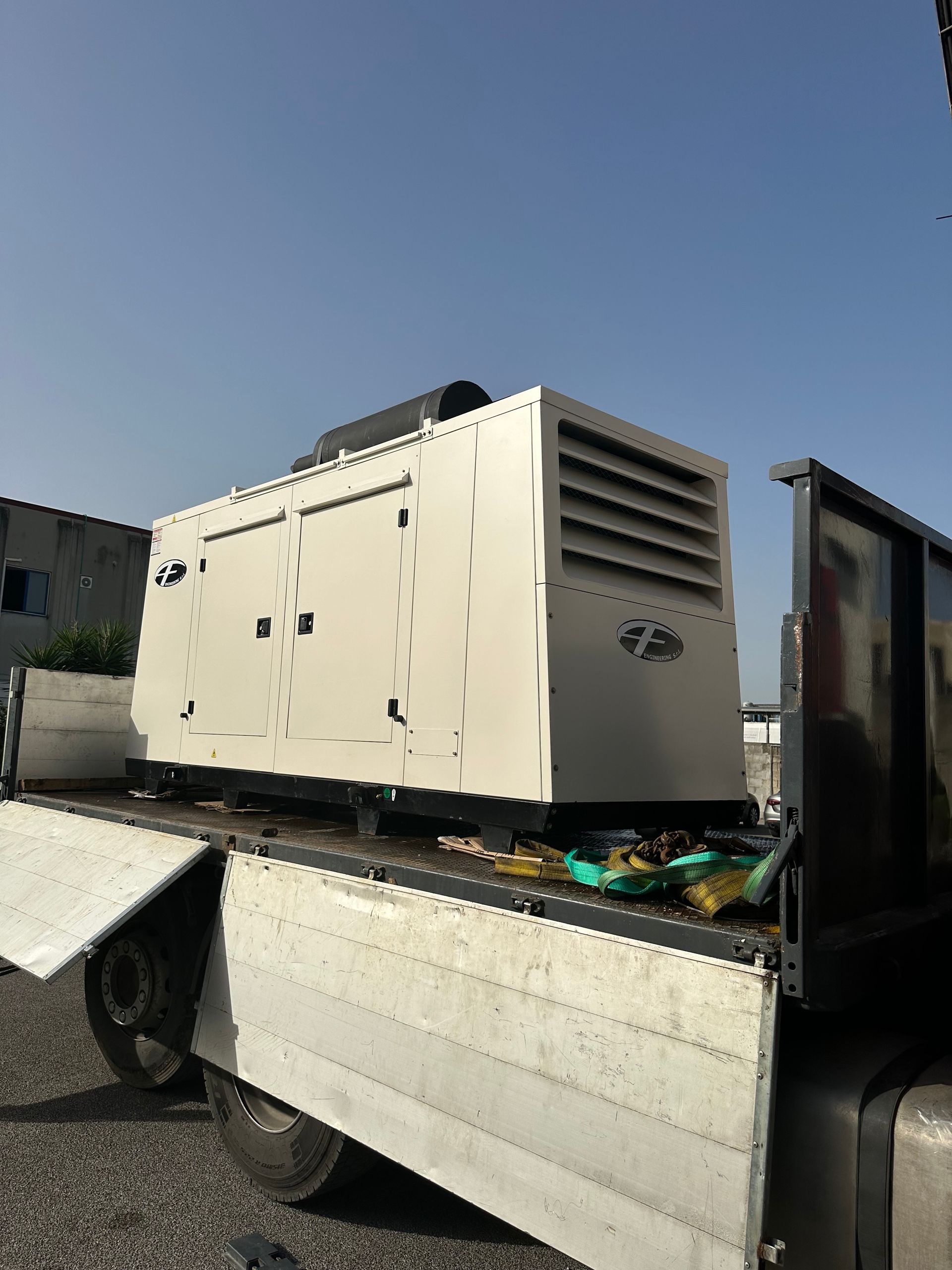 Un grande generatore bianco su un camion a pianale ribassato sotto un cielo azzurro e limpido.