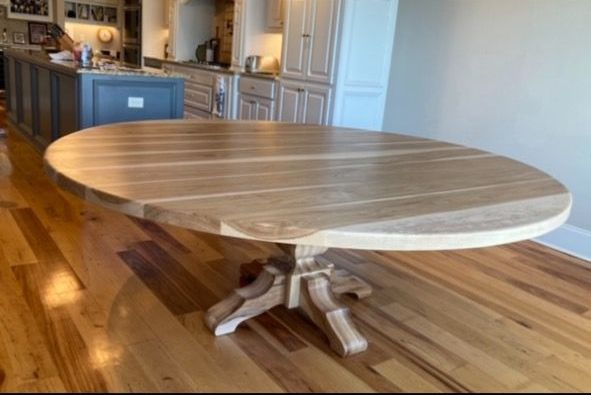 A round wooden table is sitting on a wooden floor in a kitchen.